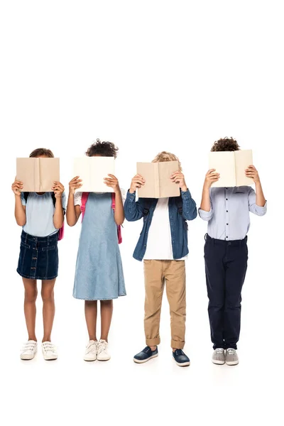 Multicultural schoolkids covering faces with books isolated on white — Stock Photo