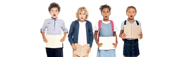 Panoramic concept of shocked multicultural schoolgirls and schoolboys holding books isolated on white — Stock Photo