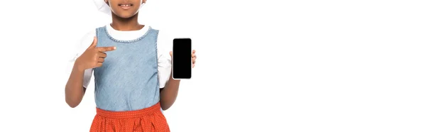 Cultivo panorámico de niño afroamericano vestido con traje de chef apuntando con el dedo al teléfono inteligente con pantalla en blanco aislado en blanco - foto de stock