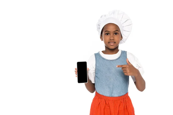 Afro-américain enfant habillé en costume de chef pointant du doigt smartphone avec écran blanc isolé sur blanc — Photo de stock
