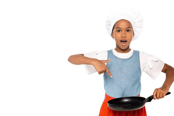 Sorpreso bambino afroamericano in costume di chef che punta con il dito alla padella isolata su bianco — Foto stock