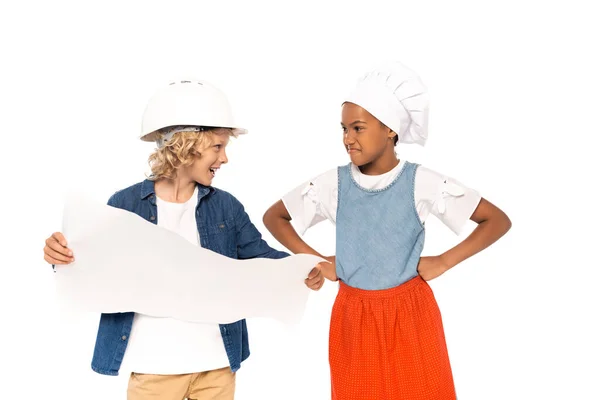 Boy in costume of architect holding blueprint and looking at displeased african american kid standing with hands on hips isolated on white — Stock Photo