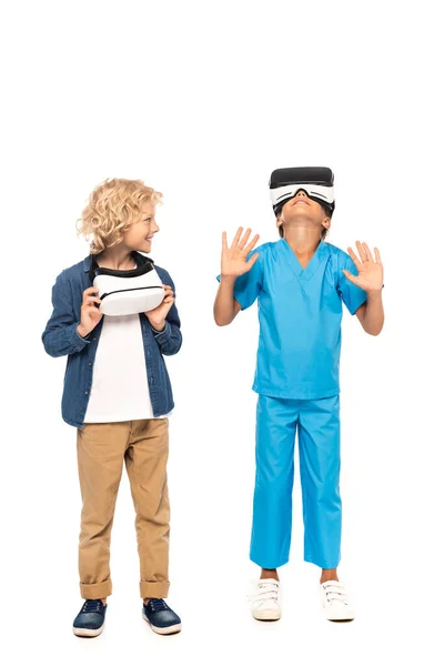 Curly boy looking at kid in virtual reality headset gesturing isolated on white — Stock Photo