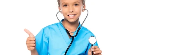 Plan panoramique d'enfant en costume de médecin tenant stéthoscope tout en montrant pouce vers le haut isolé sur blanc — Photo de stock