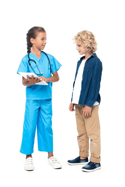 Дитина в костюмі лікаря з використанням цифрового планшета біля кучерявого хлопчика ізольована на білому — стокове фото