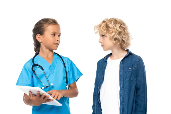 Bambino in costume di medico utilizzando tablet digitale vicino ragazzo riccio isolato su bianco — Foto stock