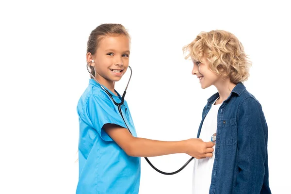Criança em traje de médico examinando menino encaracolado isolado em branco — Fotografia de Stock