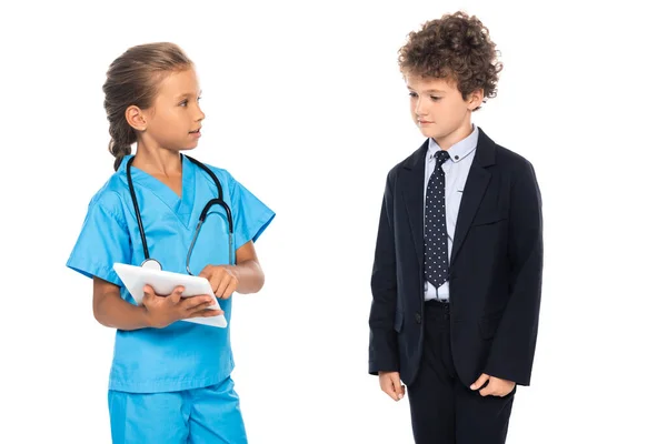 Child in costume of doctor using digital tablet near curly boy in formal wear isolated on white — Stock Photo