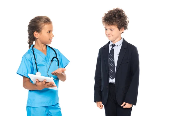 Child in costume of doctor pointing with hand at digital tablet near curly boy in formal wear isolated on white — Stock Photo