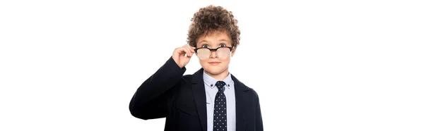 Récolte panoramique de garçon bouclé en costume touchant des lunettes et regardant la caméra isolée sur blanc — Photo de stock