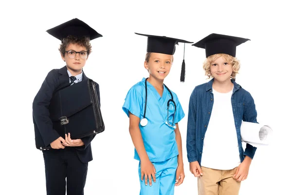 Kids in graduation caps dressed in costumes of different professions holding blueprint and briefcase isolated on white — Stock Photo