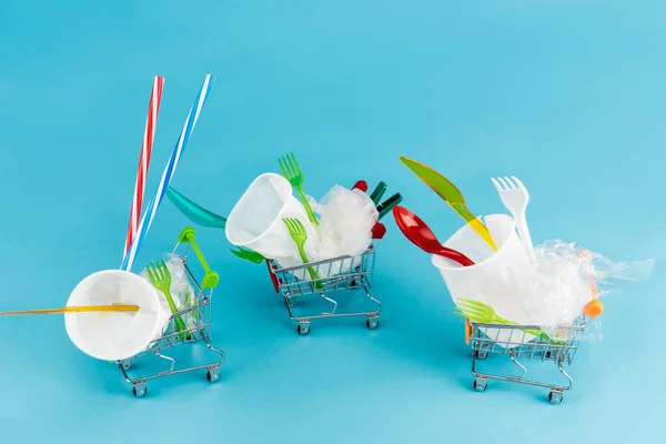 Disposable plastic objects in small shopping carts on blue background — Stock Photo