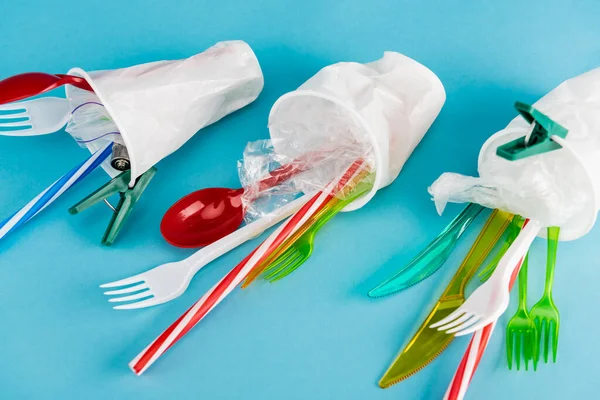 Plastic cups with disposable cutlery on blue background — Stock Photo