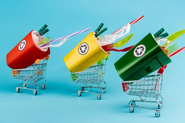 Caixas de reciclagem multicoloridas com plástico em pequenos carrinhos de compras em fundo azul — Fotografia de Stock