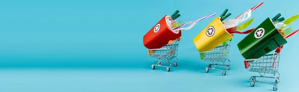 Bacs de recyclage multicolores avec plastique dans de petits chariots sur fond bleu, vue panoramique — Photo de stock