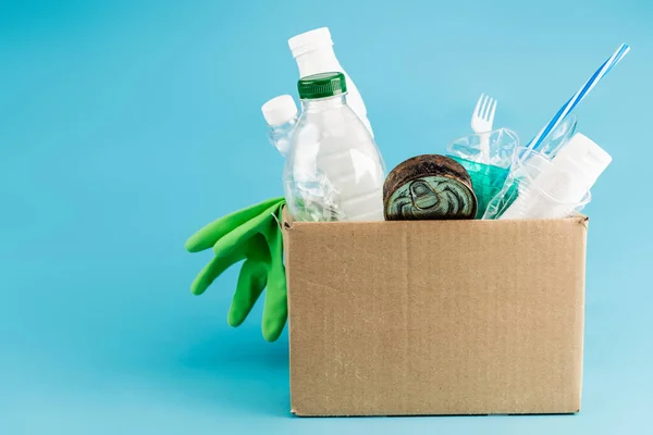 Plastic rubbish and rubber gloves in cardboard box on blue background — Stock Photo