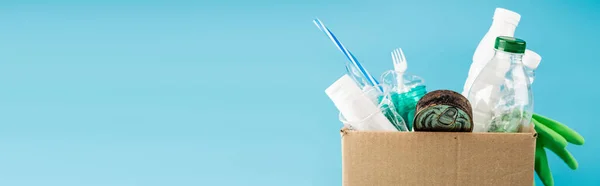 Plastic rubbish and rubber gloves in cardboard box isolated on blue, panoramic shot — Stock Photo