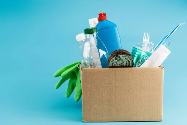 Déchets plastiques et gants en caoutchouc dans une boîte en carton sur fond bleu — Photo de stock