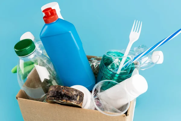 Guantes de goma y basura de plástico en caja de cartón sobre fondo azul - foto de stock