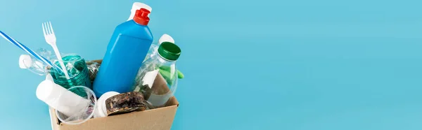 Guantes de goma y basura de plástico en caja de cartón sobre fondo azul, plano panorámico - foto de stock