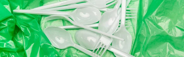 Top view of white disposable cutlery on green plastic texture, panoramic shot — Stock Photo