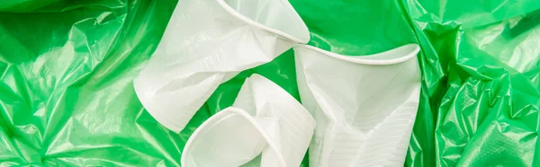Vue de dessus des tasses jetables froissées blanches sur la texture en plastique vert, vue panoramique — Photo de stock