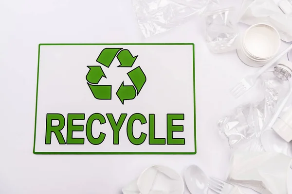 Vue du dessus de la carte de recyclage et des déchets plastiques éparpillés sur fond blanc — Photo de stock