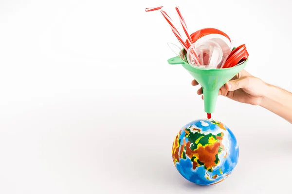 Cropped view of man holding funnel with plastic above globe on white background — Stock Photo