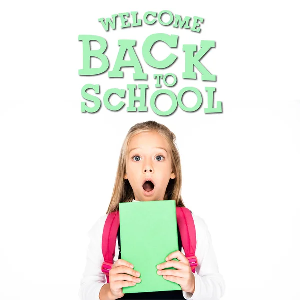 Schockiertes Schulmädchen hält Buch in der Hand, während es in die Kamera blickt, isoliert auf weiß, Willkommen zurück in der Schule — Stockfoto