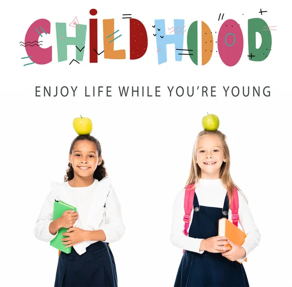 Мультикультурные школьницы с яблоками на головах, держащие книги изолированы на белом, детские иллюстрации — стоковое фото