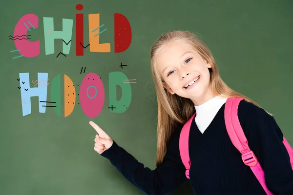 Schoolgirl pointing with finger at childhood illustration on green chalkboard — Stock Photo