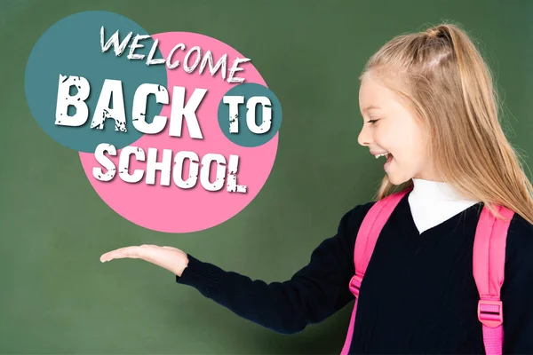 Schoolgirl pointing with hand at welcome back to school illustration on green chalkboard — Stock Photo
