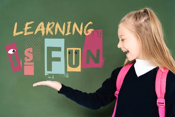 Schoolgirl pointing with hand at learning is fun illustration on green chalkboard — Stock Photo