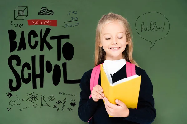 Schulmädchen liest Buch neben grüner Kreidetafel mit Illustration zur Schule — Stockfoto