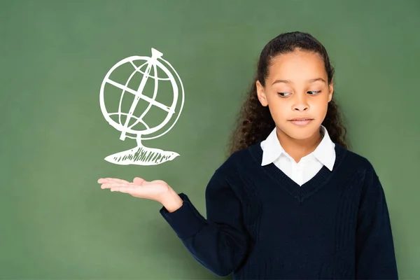 Colegiala escéptica señalando con la mano en el globo en pizarra verde - foto de stock