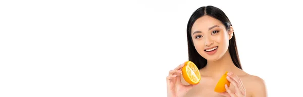 Recorte horizontal de mujer asiática desnuda mirando a la cámara mientras sostiene mitades de naranja jugosa aislada en blanco - foto de stock