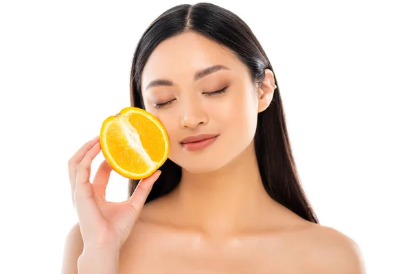 Jovem asiático mulher com fechado olhos segurando metade de suculento laranja perto rosto isolado no branco — Fotografia de Stock