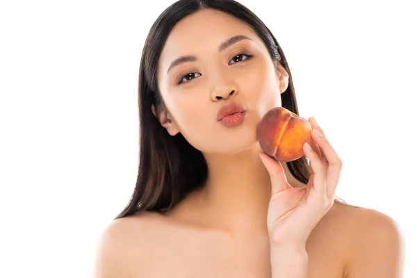 Mujer asiática desnuda haciendo pucheros labios mientras sostiene melocotón maduro cerca de la cara aislado en blanco - foto de stock