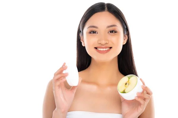 Brunette asiatique femme tenant conteneur de crème cosmétique avec la moitié de pomme isolé sur blanc — Photo de stock