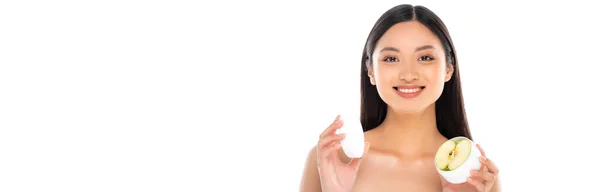 Horizontal image of young asian woman holding container of cosmetic cream with cut apple isolated on white — Stock Photo