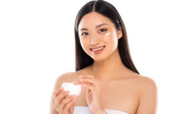 Brünette asiatische Frau berühren kosmetische Creme, während sie auf Kamera isoliert auf weiß — Stockfoto