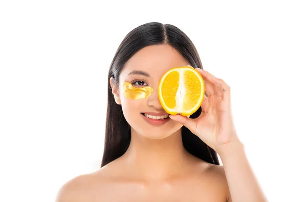 Brunette asian woman with golden cosmetic patch covering eye with half of ripe orange isolated on white — Stock Photo