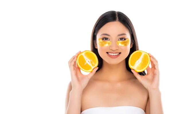 Young asian woman with golden eye patches on face holding halves of fresh orange isolated on white — Stock Photo