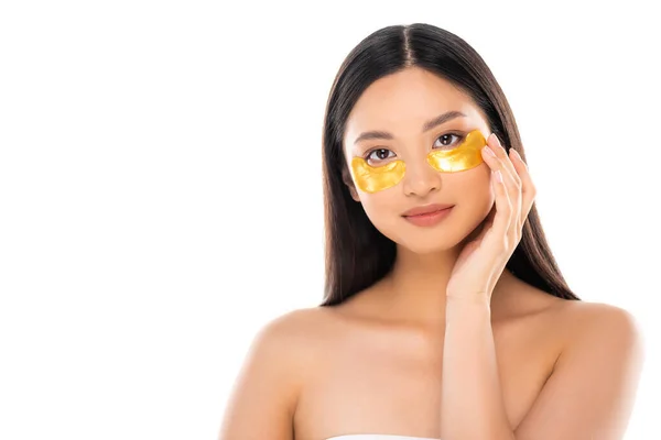 Brunetta asiatico donna toccare dorato occhio patch su faccia mentre guardando fotocamera isolato su bianco — Foto stock