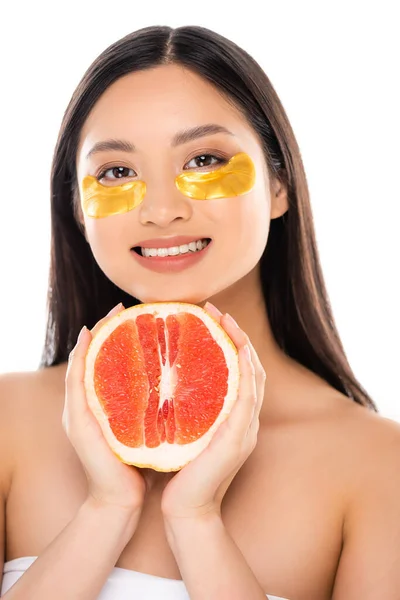 Joven asiático mujer con dorado ojo parches en cara celebración medio de jugoso manzana aislado en blanco - foto de stock