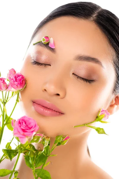 Retrato de mujer asiática sensual con los ojos cerrados, flores en la cara, cerca de pequeñas rosas aisladas en blanco - foto de stock