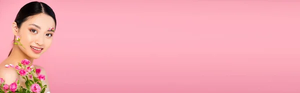 Conceito horizontal de mulher asiática com botões e pétalas no rosto e ombro, segurando minúsculas rosas isoladas em rosa — Fotografia de Stock
