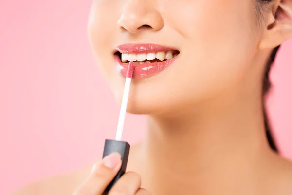 Vista recortada de la mujer joven aplicando brillo labial aislado en rosa - foto de stock