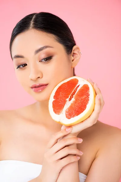 Asiatin hält Hälfte der reifen Grapefruit in Gesichtsnähe isoliert auf rosa — Stockfoto