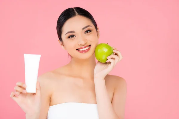 Giovane donna asiatica con crema cosmetica e mela verde matura isolata su rosa — Foto stock